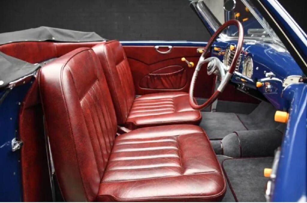 Vintage car interior with red leather seats and wooden steering wheel.