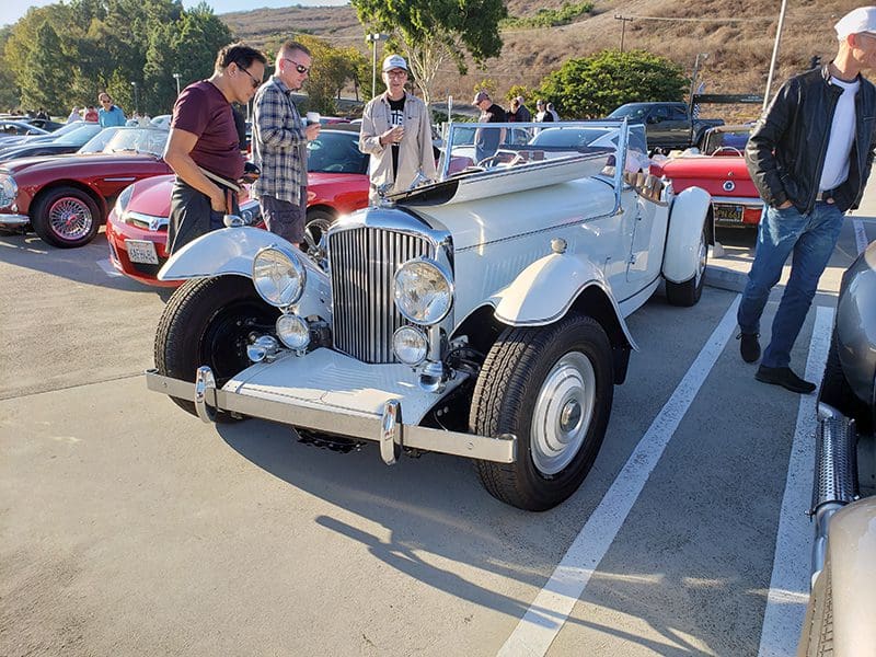 Classic silver vintage convertible car parked outdoors with people admiring it.
