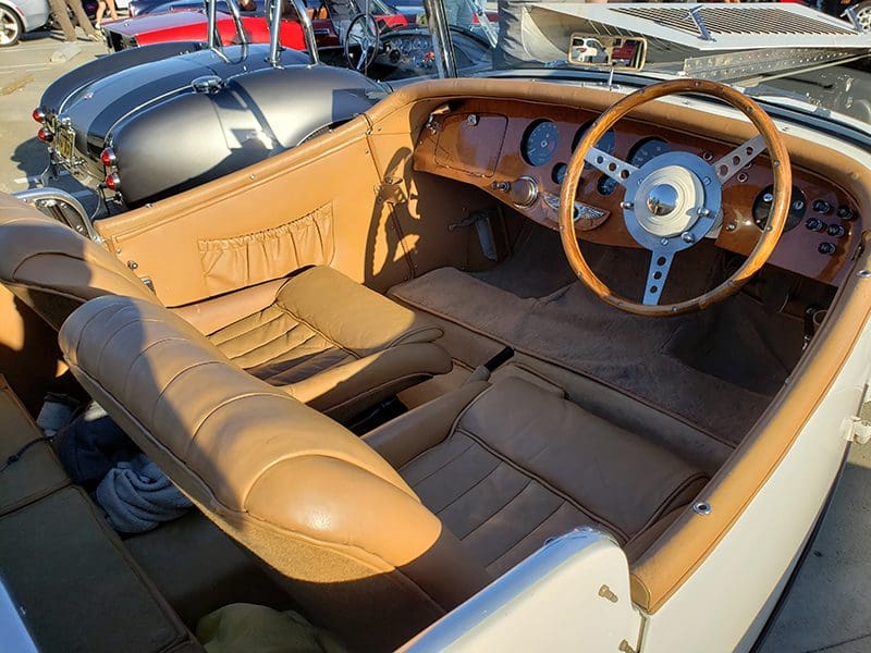 Interior of a classic car with tan leather seats and wooden dashboard.