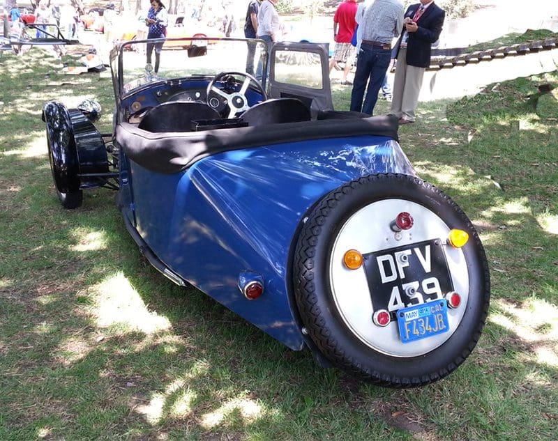Vintage blue three-wheeled car with spare tire on the back.