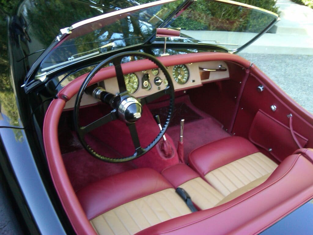 Vintage car interior with red leather seats and classic steering wheel.