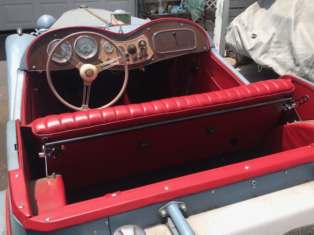 Close-up of a vintage car's red leather interior and wooden steering wheel.