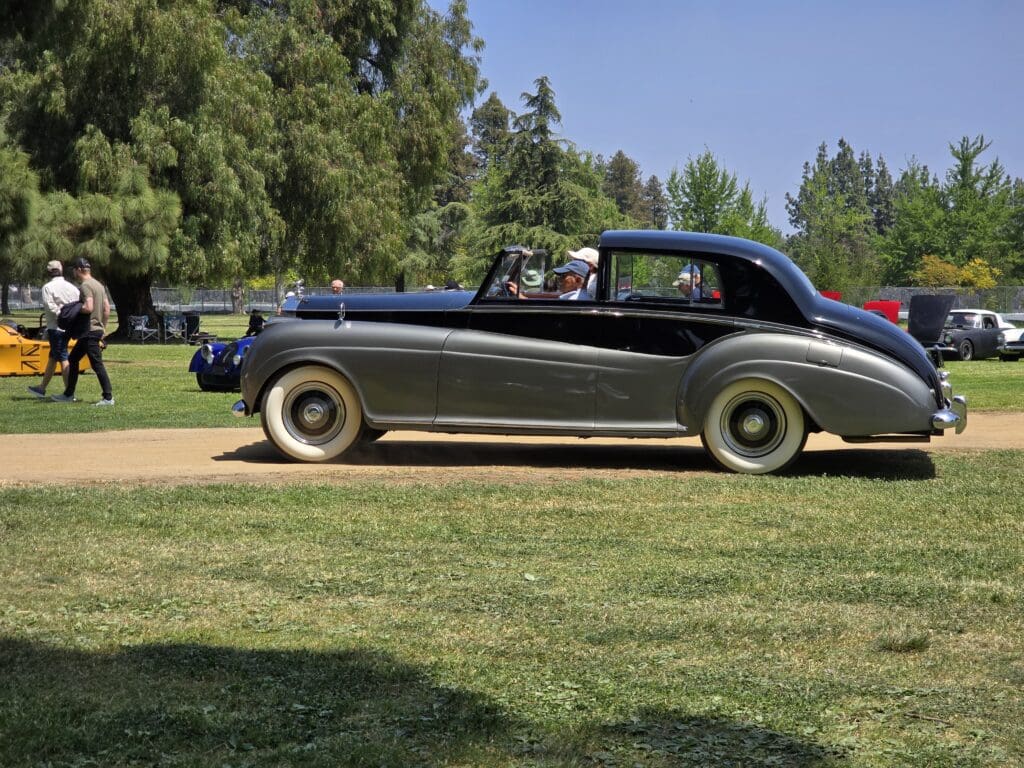 Classic black vintage car parked on grass with trees in the background.
