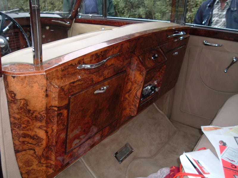 Classic car interior with polished wood dashboard and beige upholstery.