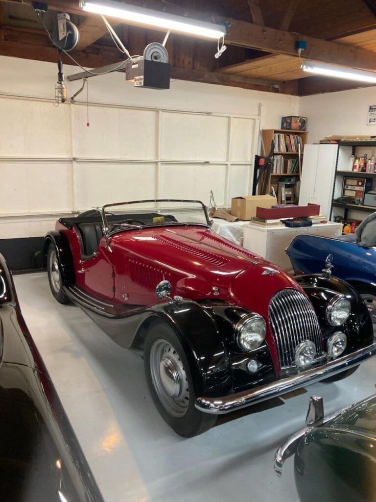 Classic red convertible sports car in a garage with other vintage vehicles.