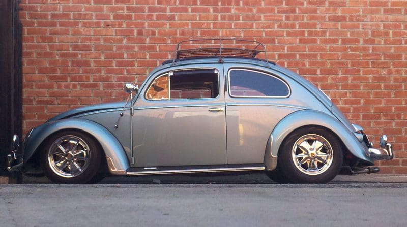 Classic silver Volkswagen Beetle parked against a brick wall.