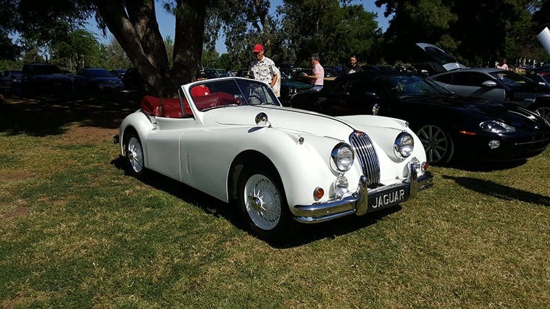 Classic white convertible car parked on grass with people nearby.