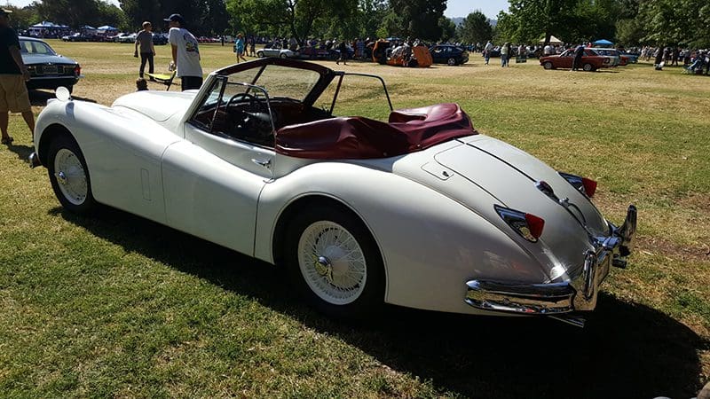 Classic white convertible car parked on grass under sunlight.