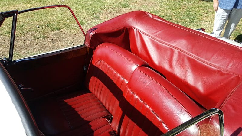 Close-up of a vintage car's red leather interior with bench seating.