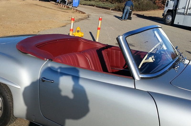 Shadow of a person on a silver convertible car near traffic cones.