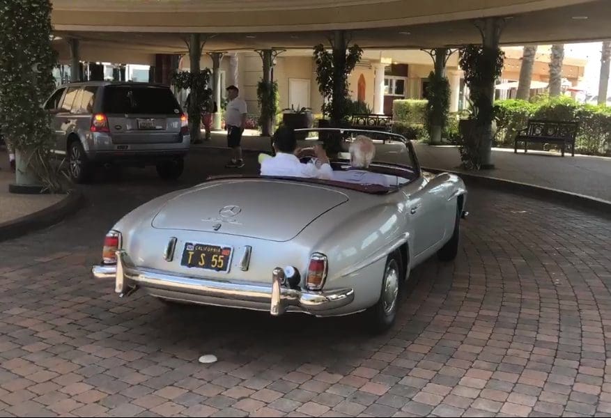 Classic white convertible car parked under a covered driveway.