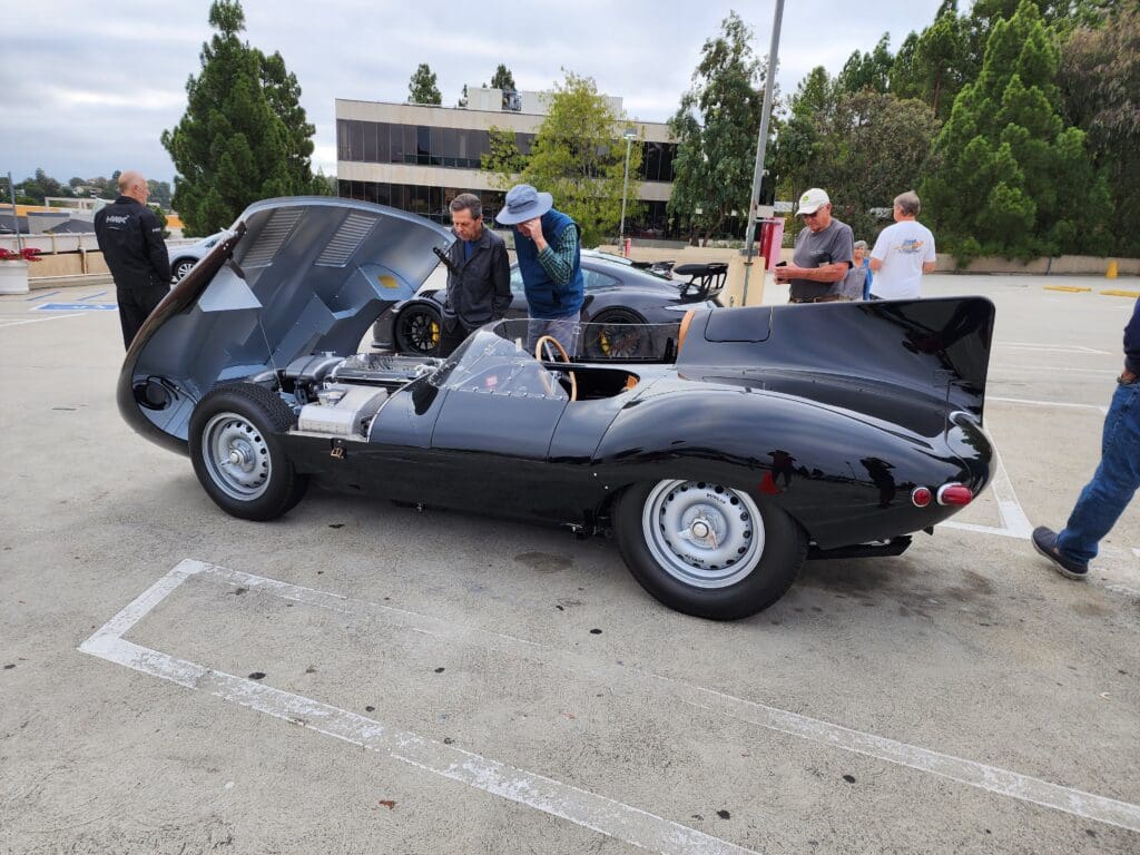 A sleek black convertible sports car parked outdoors with people around.