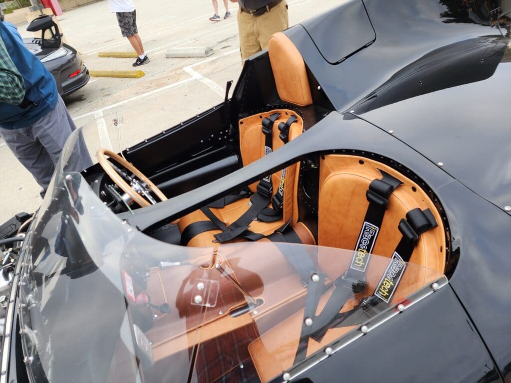 Close-up of a vintage car's open cockpit with brown leather seats and wooden details.
