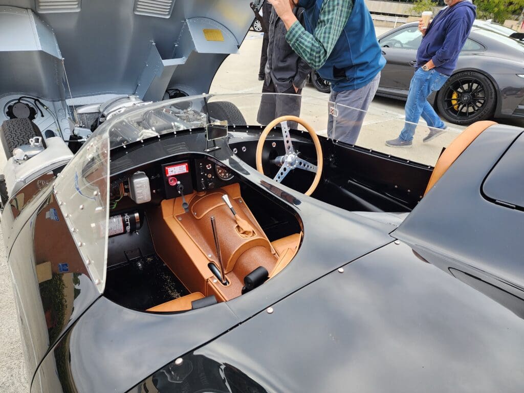 Interior of a vintage racing car with a leather seat and wooden steering wheel.