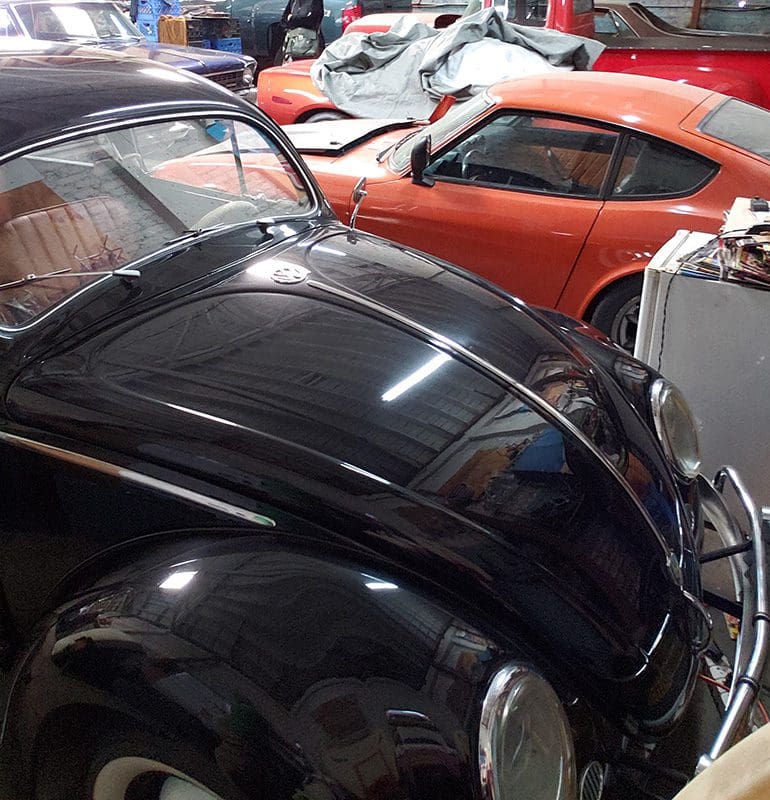 Classic black Volkswagen Beetle with a red sports car in the background.