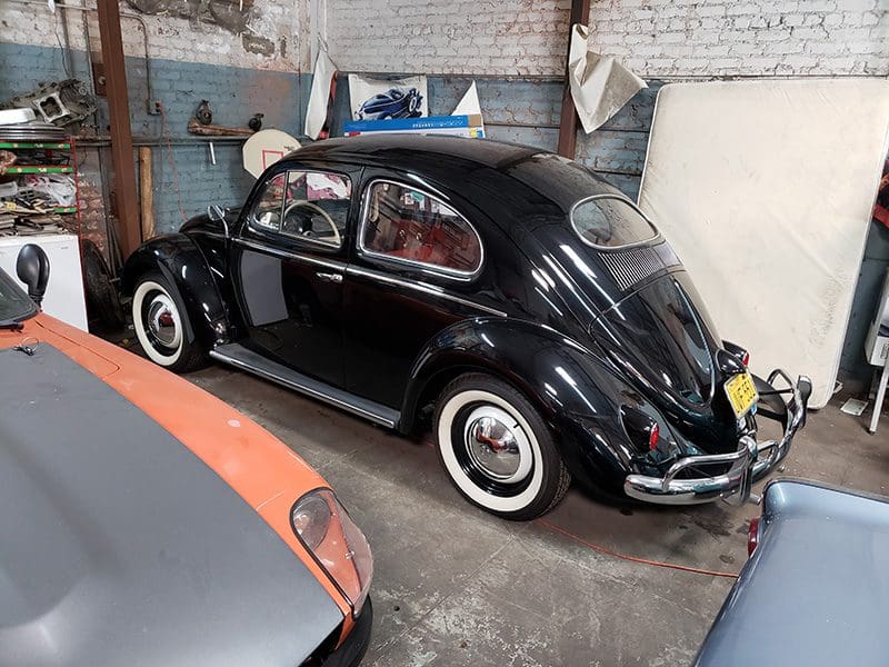 A classic black vintage car parked indoors next to other vehicles.