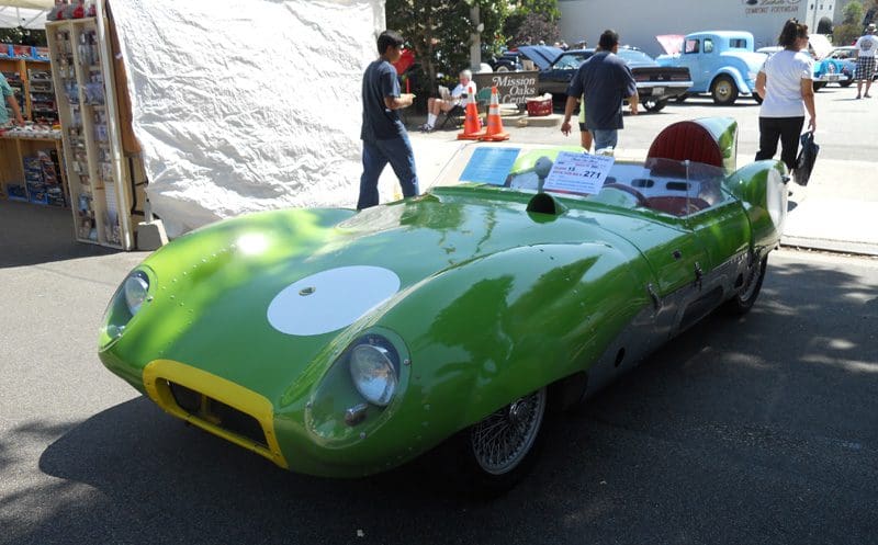 A vintage green race car parked outdoors with a driver nearby.