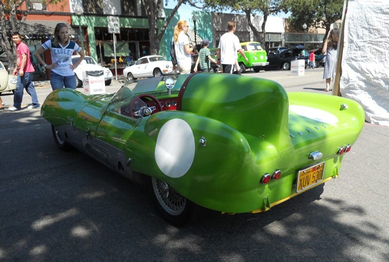 A vintage green race car parked outdoors with a driver nearby.