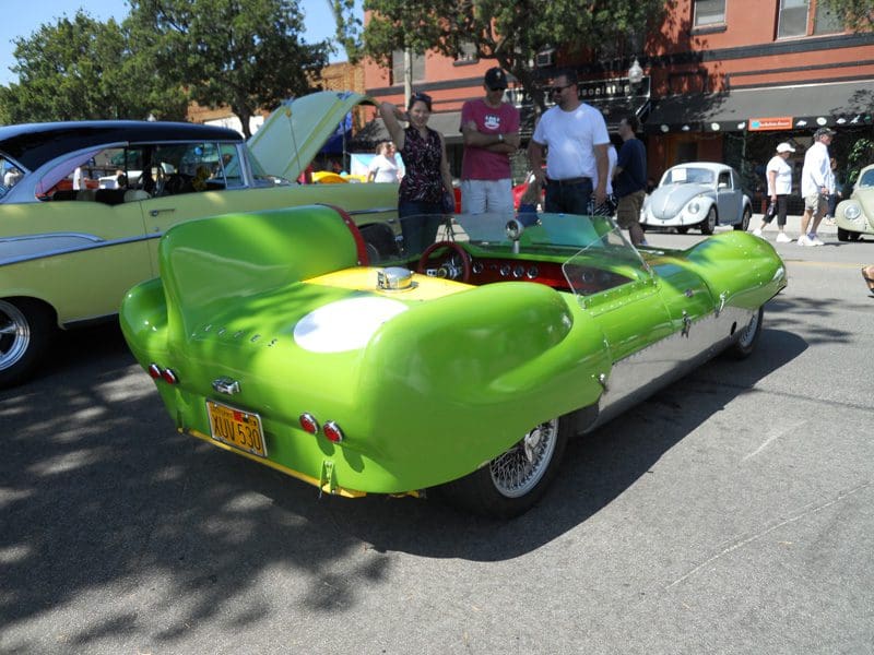 Bright green vintage car with its hood open at a sunny outdoor car show.