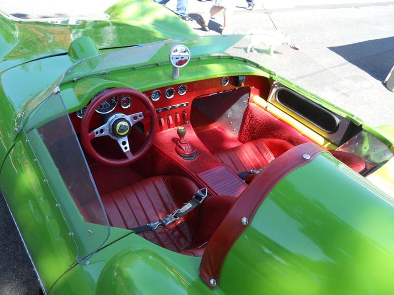 Interior of a vintage green sports car with red leather seats and classic steering wheel.