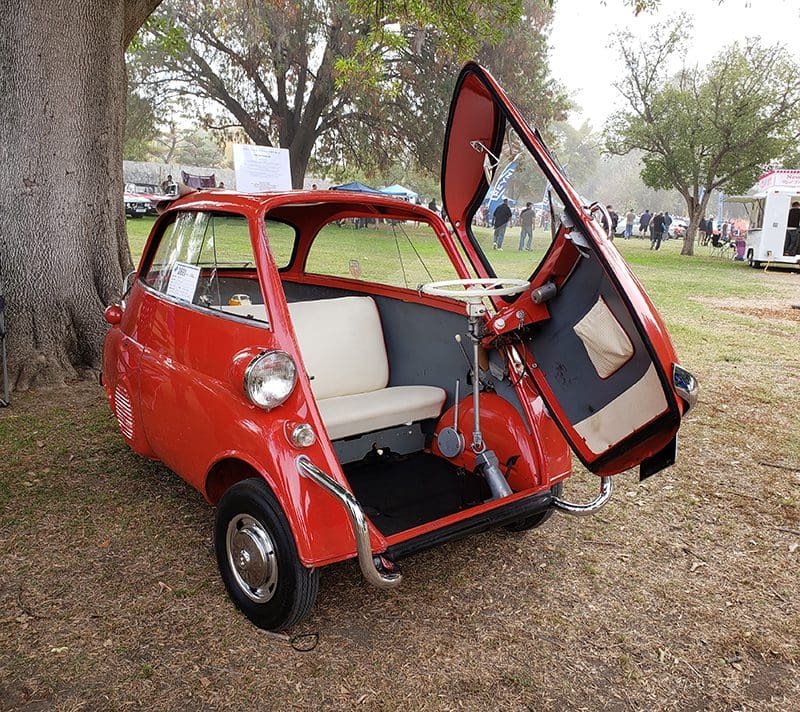 A vintage red microcar with its front door open, showing the interior.