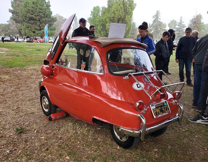 A small vintage three-wheeled car with gull-wing doors open.