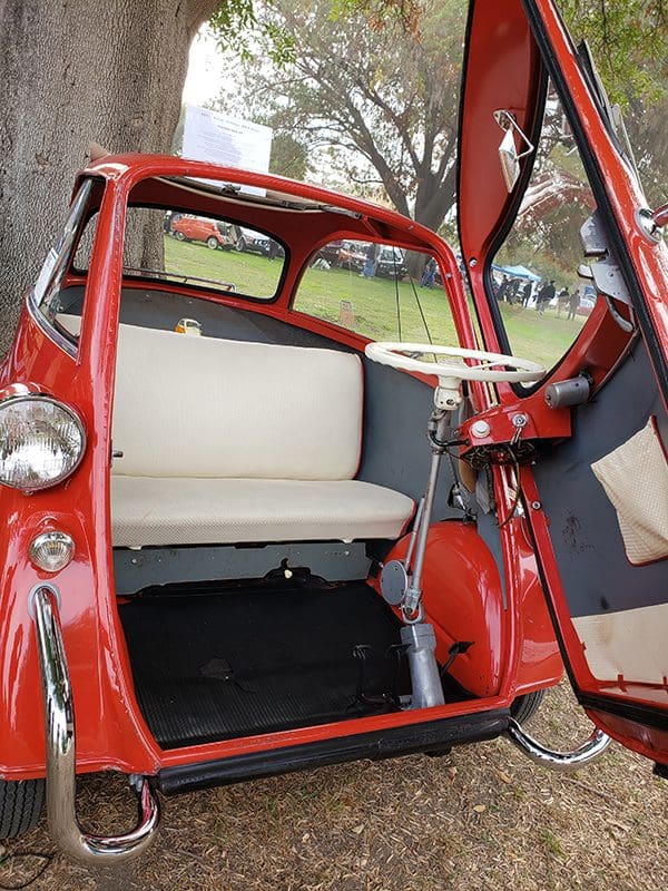 Red vintage microcar with open door and white bench seat.