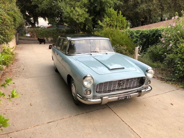Classic light blue vintage car parked on a driveway with greenery around.