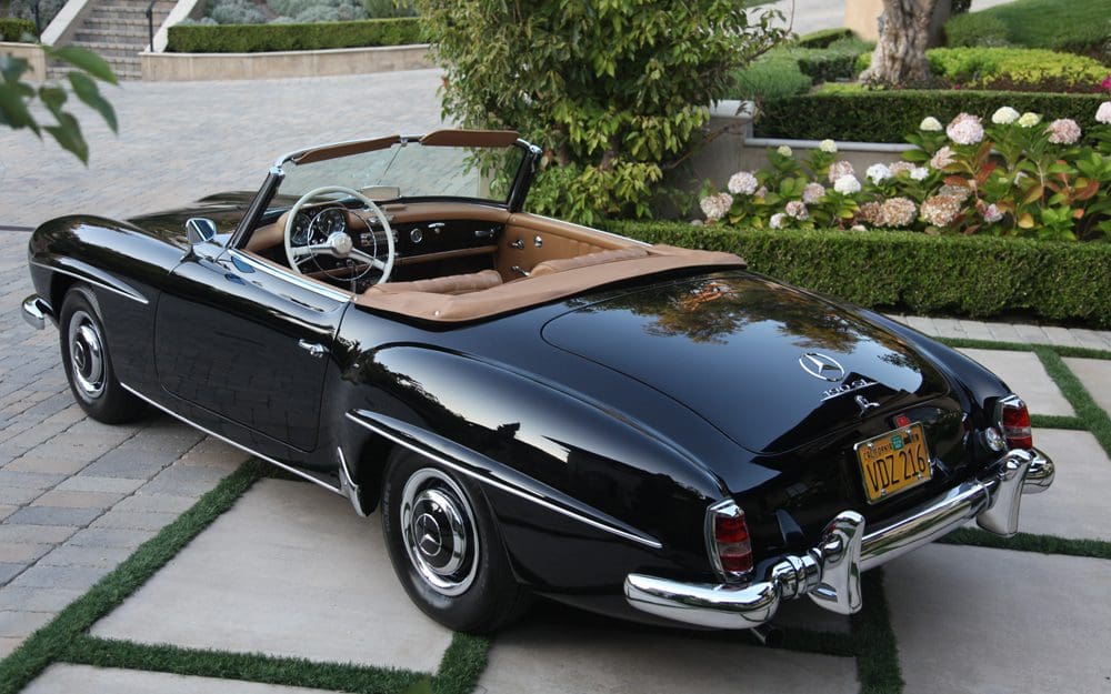 Classic black convertible car parked on a driveway with greenery.