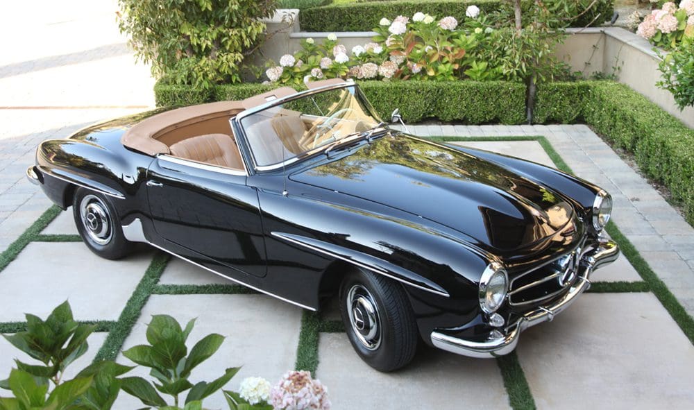 Classic black convertible car parked in a garden setting.