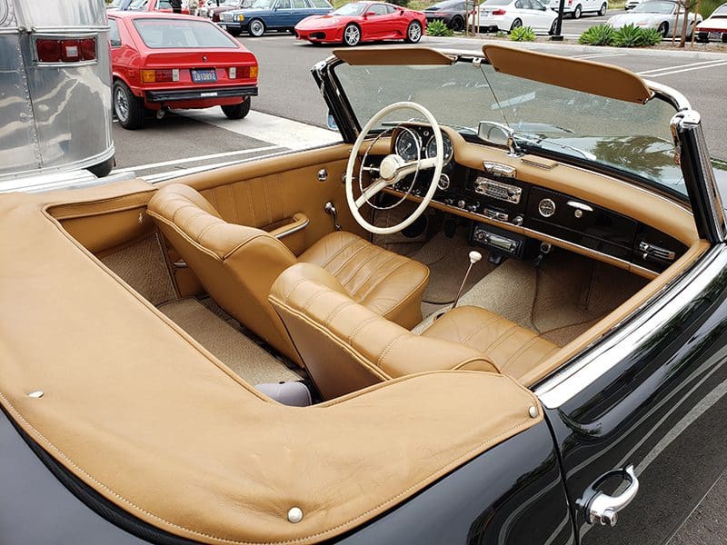 Interior of a classic convertible car with tan leather seats and wooden dashboard.