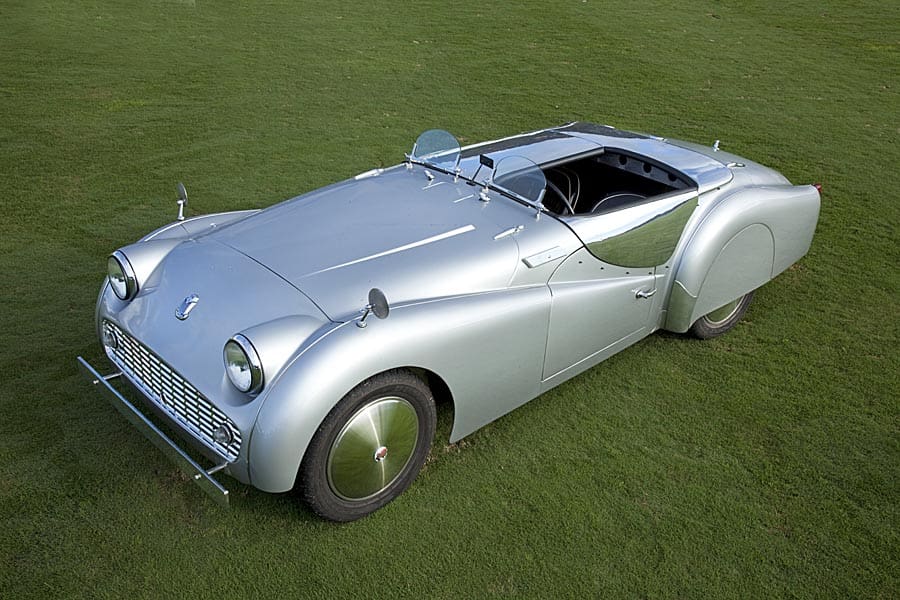 A sleek silver vintage convertible car on grass.