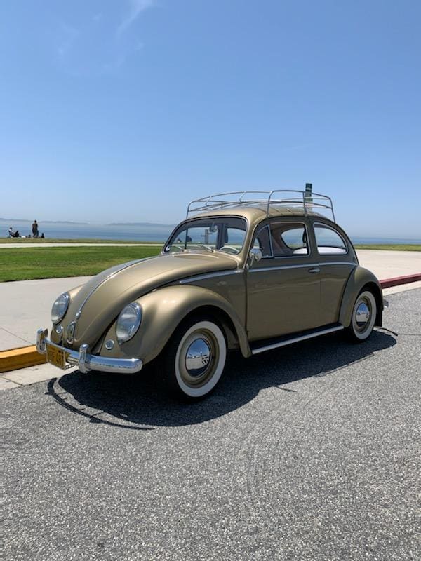 Classic beige Volkswagen Beetle parked by the seaside on a sunny day.