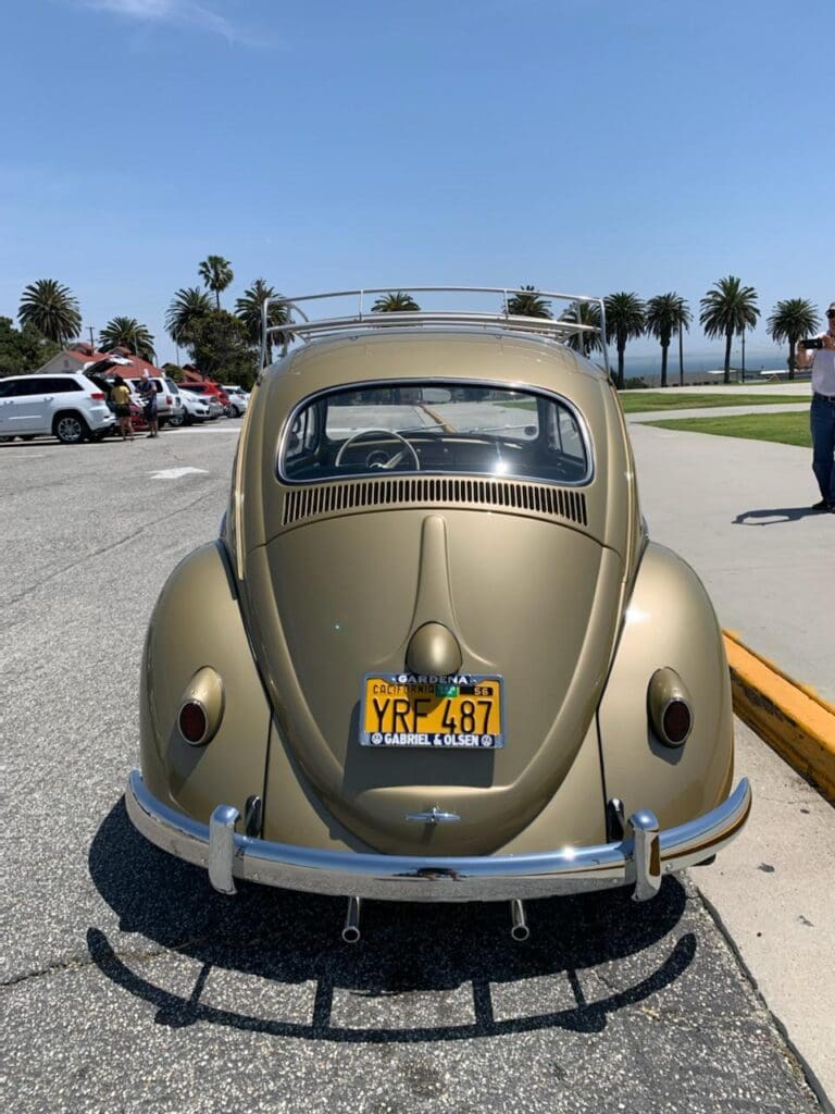 Rear view of a vintage gold Volkswagen Beetle parked near palm trees.