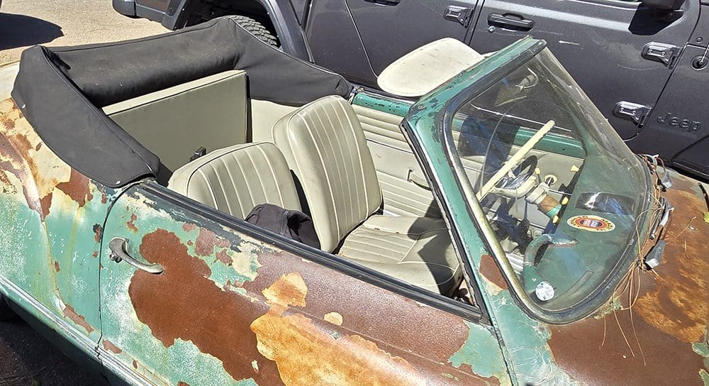 Rusty vintage convertible car parked outdoors on a sunny day.