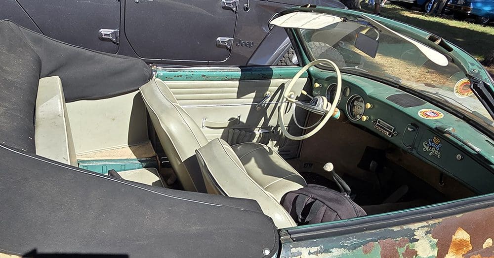 Rusty vintage convertible car parked outdoors on a sunny day.