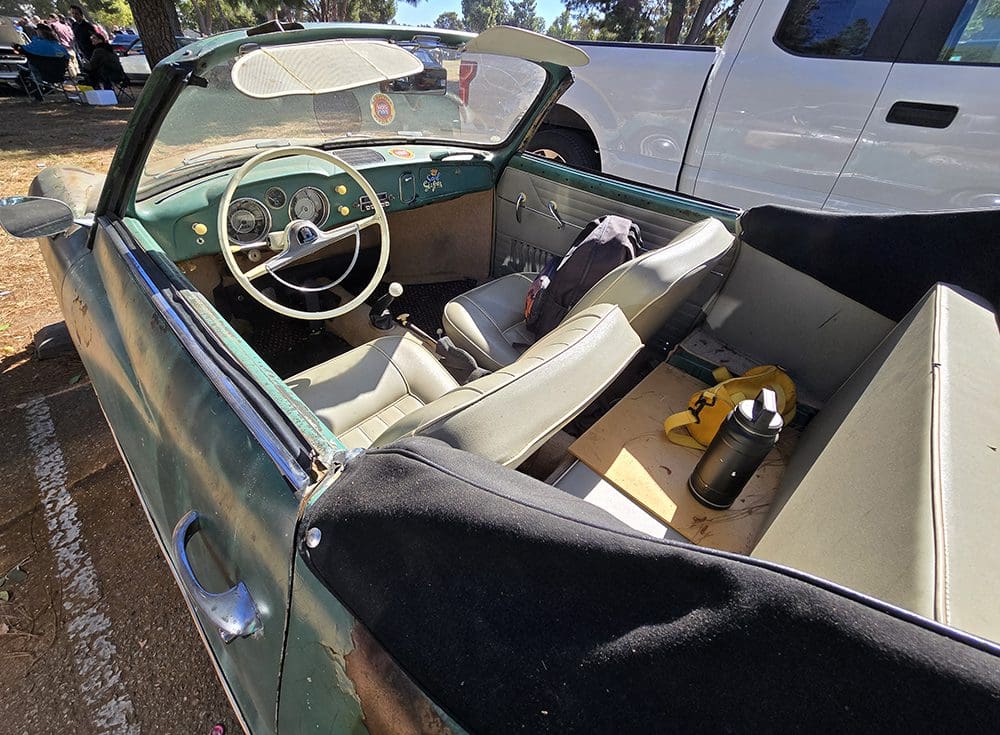 Rusty vintage convertible car parked outdoors on a sunny day.