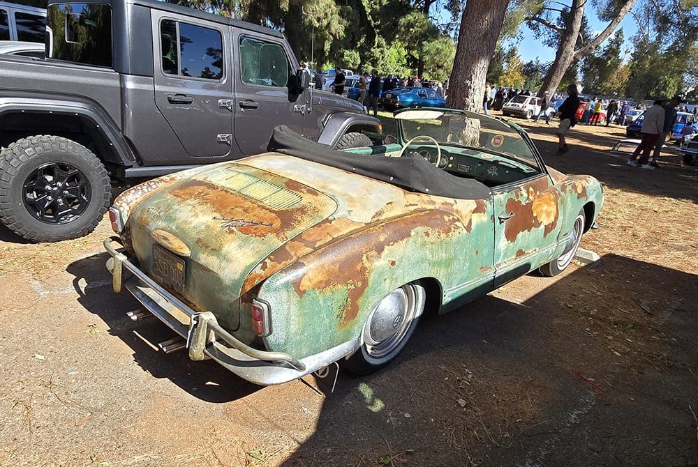 Rusty, old convertible car parked outdoors under trees.
