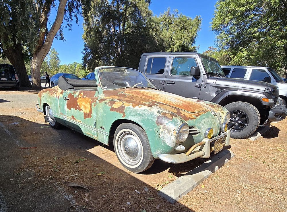 Rusty vintage convertible car parked outdoors under the sun.
