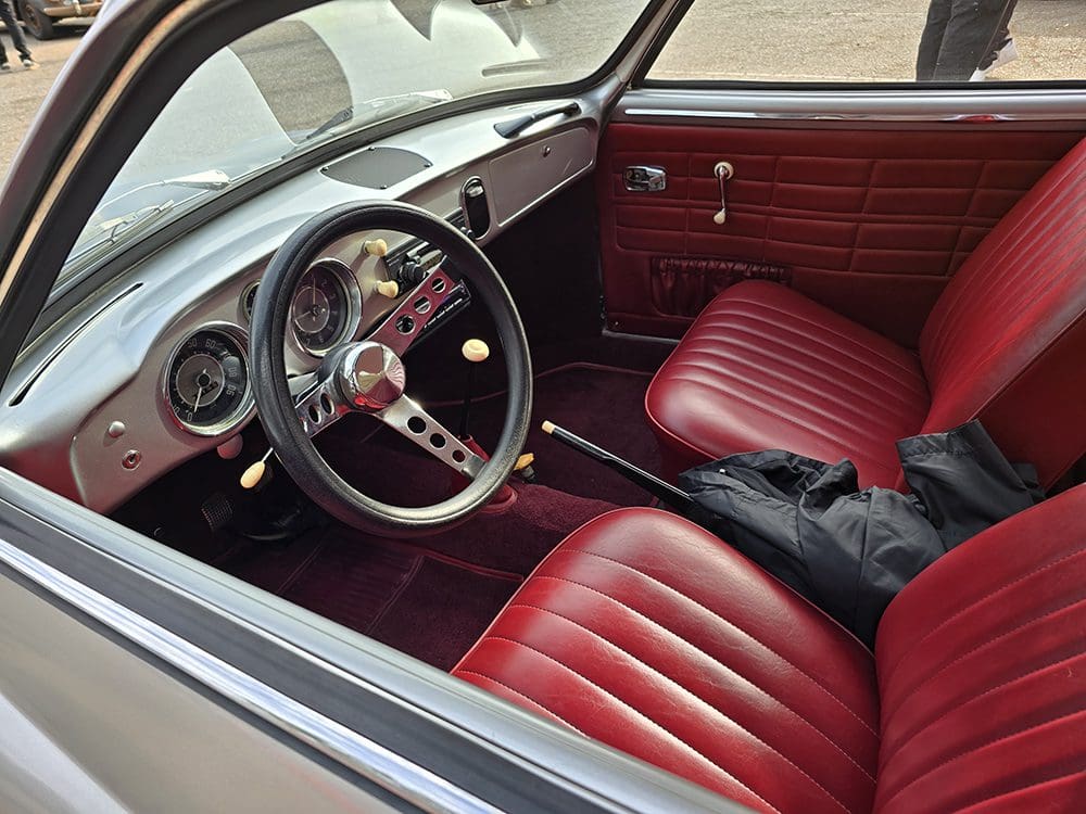 Interior of a classic car with red leather seats and a wooden steering wheel.