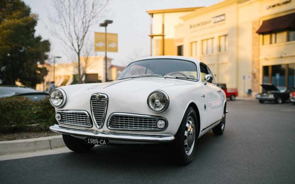 Classic white Alfa Romeo car parked on a street during golden hour.