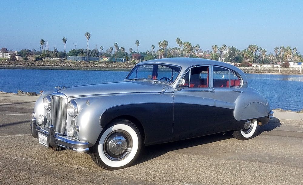 Classic silver and navy blue vintage car parked near the beach.
