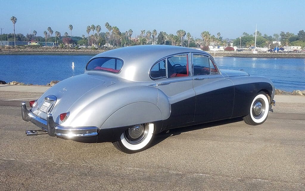 Classic silver and black vintage car parked outdoors on a sunny day.
