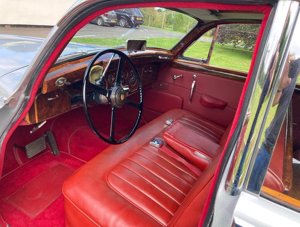 Vintage car interior with red leather seats and wooden dashboard.