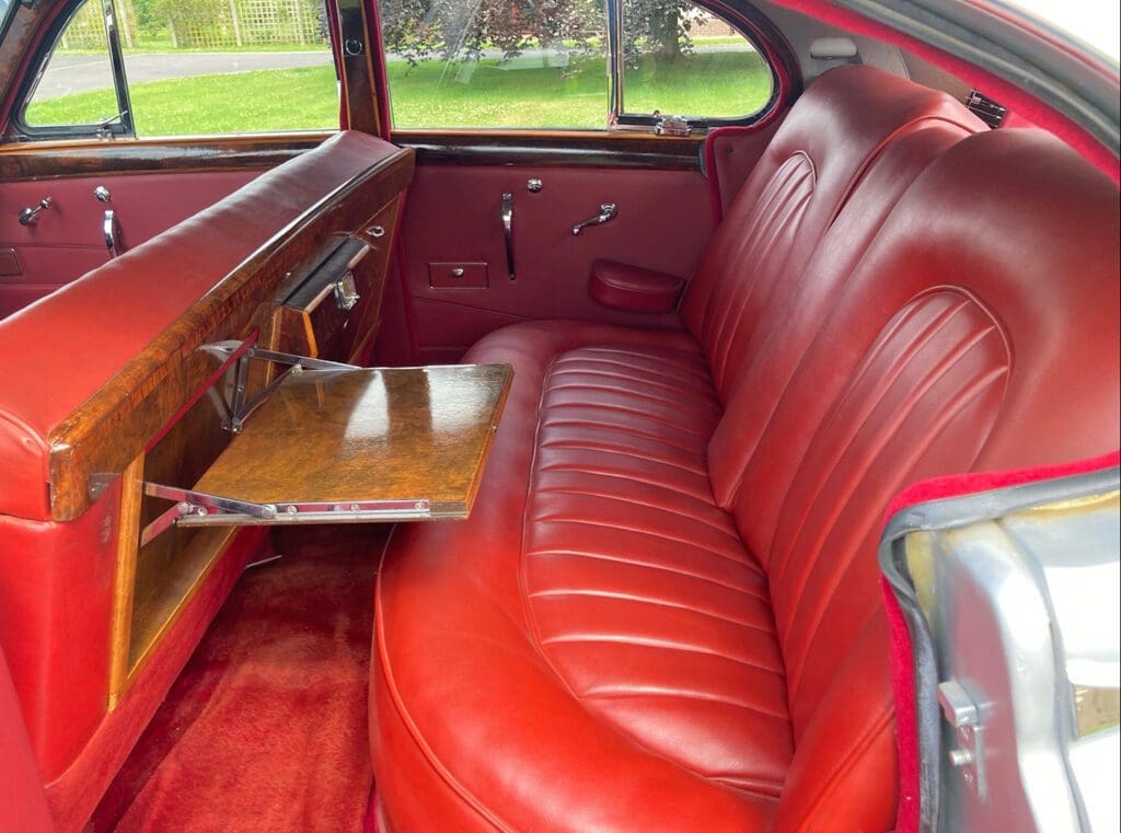 Vintage car interior with red leather seats and a fold-out wooden tray.