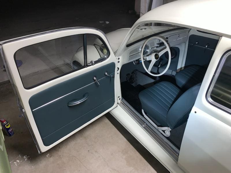 Open door view of a vintage car interior with blue seats and white steering wheel.