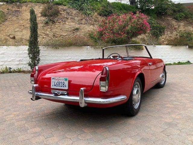 Classic red convertible car parked on a brick driveway.