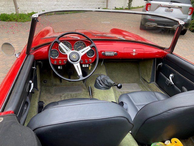 Interior of a classic red convertible car with vintage steering and dashboard.