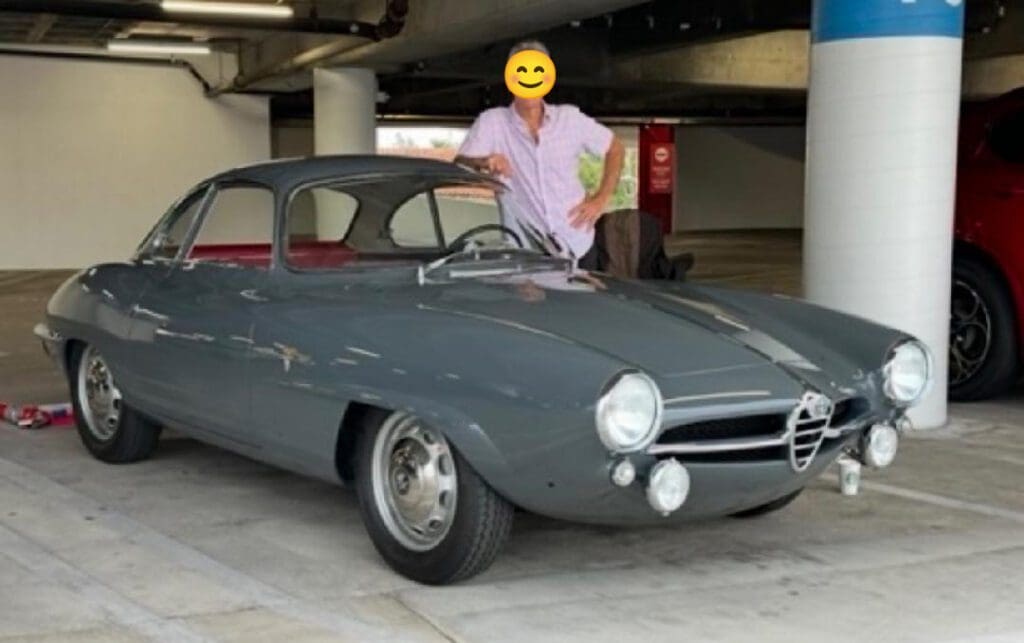 Person posing with a classic gray vintage car in a garage.