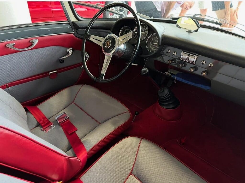 Classic car interior with red and beige upholstery and a vintage steering wheel.